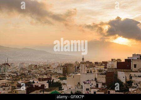 Un coucher de soleil sur Tétouan d'une lumière dorée et les montagnes couvertes de nuages. Vous pouvez également voir une mosquée. Banque D'Images