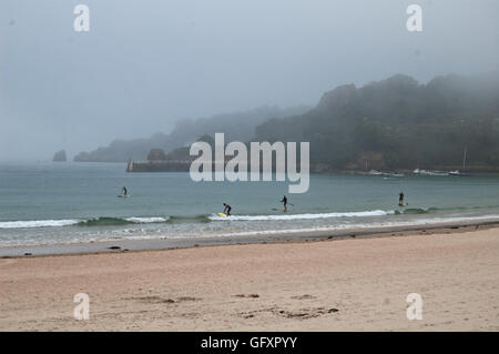 Paddleboarders dans la mer à St Brelade's bay, Jersey, comme le brouillard de mer en rouleaux Banque D'Images