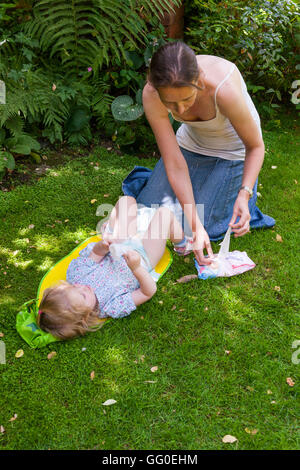 Ma mère parent accompagnant l'évolution des couches lavables nappy change de bébé tout-petit. Jardin plein air / Extérieur / Extérieur / plein air / outdoor Banque D'Images