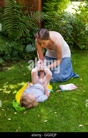 Ma mère parent accompagnant l'évolution des couches lavables nappy change de bébé tout-petit. Jardin plein air / Extérieur / Extérieur / plein air / outdoor Banque D'Images