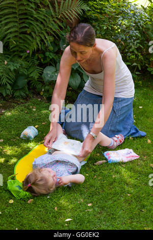 Ma mère parent accompagnant l'évolution des couches lavables nappy change de bébé tout-petit. Jardin plein air / Extérieur / Extérieur / plein air / outdoor Banque D'Images