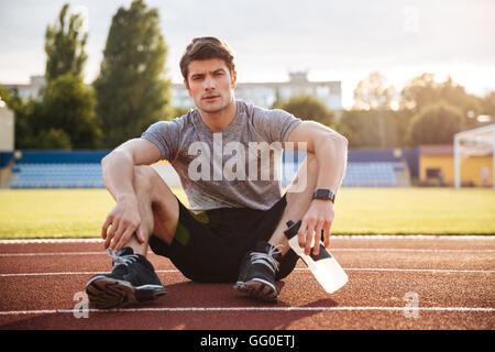 Jeune homme séduisant au repos de l'athlète dans le stade et l'eau potable Banque D'Images