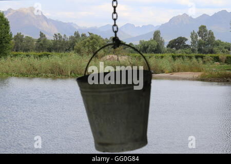 Seau pendant vers le bas sur une chaîne avec le lac et les montagnes en arrière-plan sur les vins Domaine De Vredenheim, Stellenbosch, Afrique du Sud Banque D'Images