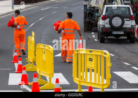 Les hommes en vêtements de travail haute visibilité orange fluo éteindre les cônes de circulation et les obstacles sur la route. Banque D'Images