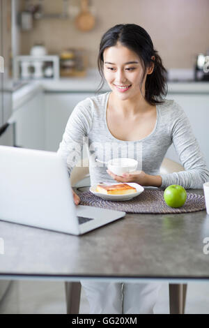 Jeune femme chinoise à l'aide d'ordinateur portable pendant le petit-déjeuner Banque D'Images