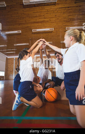 Professeur de sport et l'école les enfants formant part pile dans de basket-ball Banque D'Images