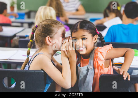 Lycéenne chuchotant à son ami s'oreille par classe Banque D'Images