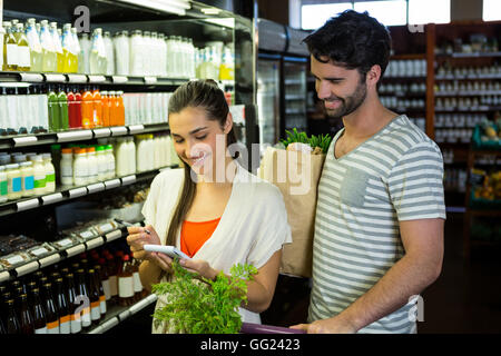 La femme et l'homme contrôle de leur bloc-notes pendant leurs achats dans la section bio Banque D'Images