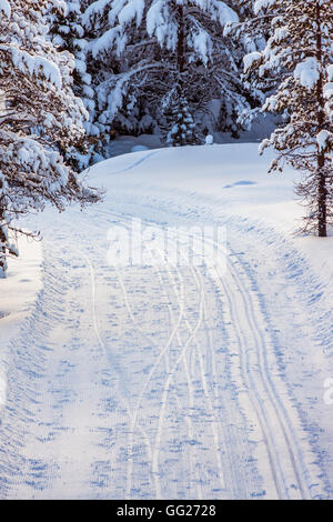 Une machine faite en piste sur la droite, et les pistes de ski sur le plat de la route sur la gauche, visible dans la neige. Banque D'Images