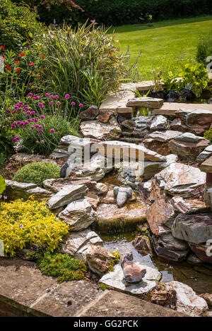 Une petite cascade en pierre dans un jardin anglais avec des fleurs d'accompagnement Banque D'Images