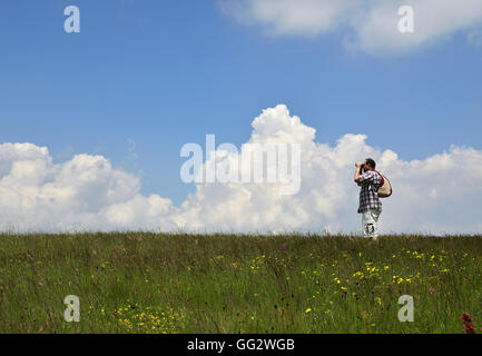 L'homme avec un sac à dos et des jumelles dans un pré et l'observation de l'environnement à travers les jumelles. Banque D'Images