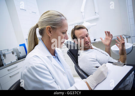 Femme dentiste writing on clipboard lors de l'interaction avec male patient Banque D'Images