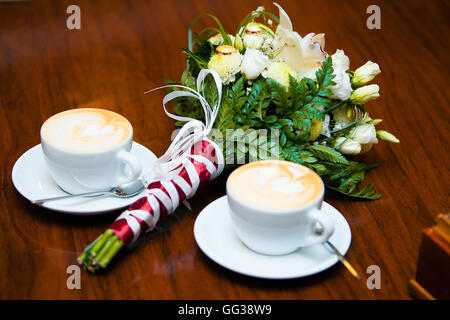 Mariage de deux tasses de café avec de la crème fouettée. Bouquet de mariée et deux anneaux de mariage Banque D'Images