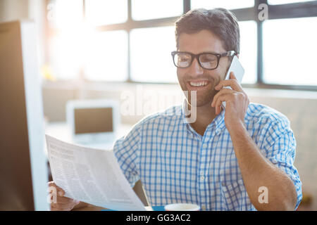 Homme d'affaires talking on mobile phone while reading newspaper Banque D'Images