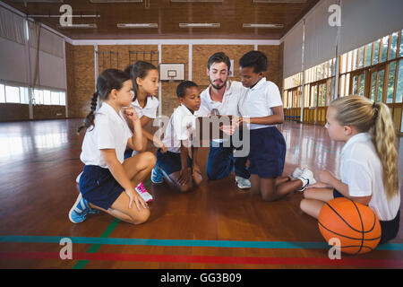 Professeur de sport et l'école les enfants à discuter sur le presse-papiers dans la région de basket-ball Banque D'Images