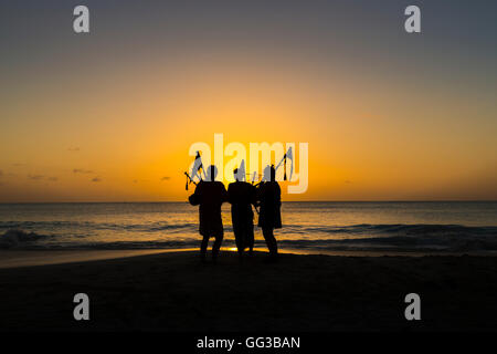 Cornemuse cornemuse jouant sur la plage au coucher du soleil à Jolly Harbour, au sud-ouest de l'Antigua Banque D'Images