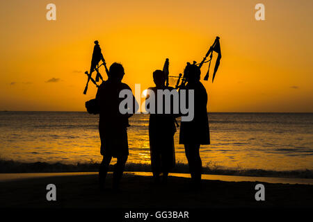 Cornemuse cornemuse jouant sur la plage au coucher du soleil à Jolly Harbour, au sud-ouest de l'Antigua Banque D'Images