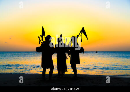 Cornemuse cornemuse jouant sur la plage au coucher du soleil à Jolly Harbour, au sud-ouest de l'Antigua Banque D'Images