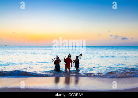 Pataugeant dans la mer les gaiteiros jouant de la cornemuse sur la plage au coucher du soleil à Jolly Harbour, au sud-ouest de l'Antigua Banque D'Images