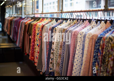 Ligne de chemises colorées sur un rack / rail dans un magasin, de nombreux avec des motifs. Banque D'Images