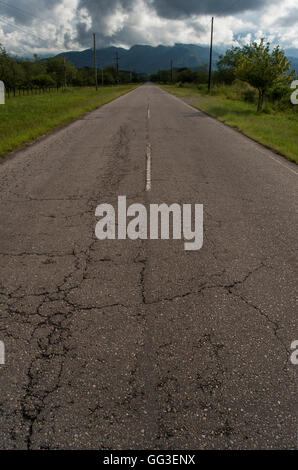 Quelque peu détériorée vieille route à travers la campagne, montagnes et nuages dans l'arrière-plan Banque D'Images