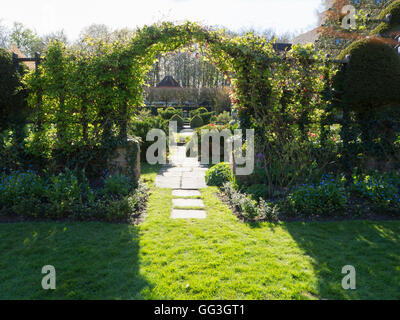 Soleil et ombre à travers le treillis arch avec pavage menant à Chenies Manor jardin en contrebas au printemps.un jardin accueillant. Banque D'Images