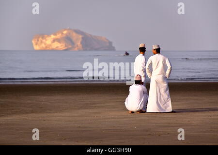 Trois hommes habillés de façon traditionnelle omanaise sur la plage principale dans le centre de Mascate, Oman, coucher du soleil Banque D'Images