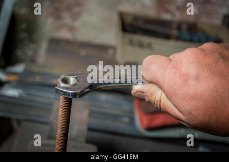 Main travailleur serrer ou desserrer un écrou d'un boulon rouillé avec une clé sur fond blanc Banque D'Images