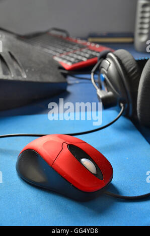 Souris à molette rouge et mat, casque, ordinateur et le clavier s'asseoir sur un bureau. En tête bleu Banque D'Images