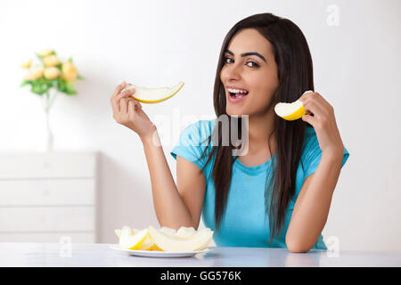 Portrait of beautiful young woman eating cantaloupe à la maison Banque D'Images