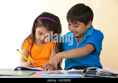 Cute boy aider sœur dans ses devoirs à la table contre l'arrière-plan de couleur Banque D'Images