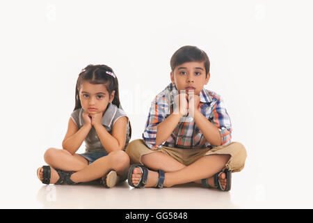 Portrait de la fratrie ennuyé assis contre fond blanc Banque D'Images
