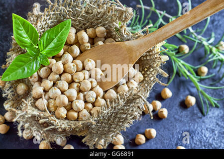 Garbanzo (pois chiches) et cuillère en bois avec du basilic dans de petits sac de toile sombre sur fond rustique. Top View with copy space Banque D'Images