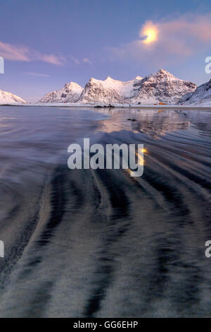 Pleine lune reflétée dans la mer de glace autour de la plage de Skagsanden surréaliste, Flakstad, comté de Nordland, îles Lofoten, Norvège Banque D'Images