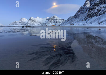 Pleine lune reflétée dans la mer de glace autour de la plage de Skagsanden surréaliste, Flakstad, comté de Nordland, îles Lofoten, Norvège Banque D'Images