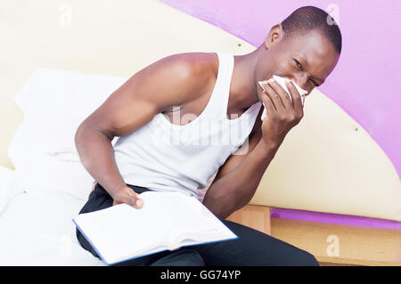 Ce jeune homme assis sur un lit et tenant une bible un rhume Banque D'Images