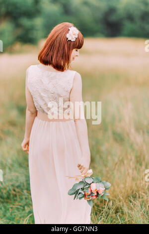 Jeune fille dans une robe de mariée blanche avec bouquet de fleurs roses et verts se dresse sur prairie dans les bois Banque D'Images