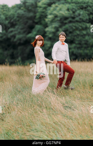 Mariée et le marié à marcher ensemble main dans la main sur une magnifique prairie d'été en fleurs Banque D'Images