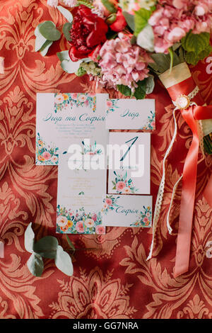 Vue de dessus de pivoines rose verdure avec les invitations de mariage sur fond rouge Banque D'Images