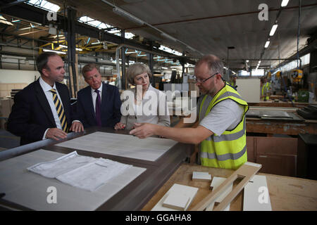 Premier ministre Theresa May avec Martek Gérant Derek Galloway (2e à gauche) et Croydon MP Centrale Gavin Barwell (gauche) Parlez à un travailleur au cours de sa visite à Martek de menuiserie à New Addington, Surrey. Banque D'Images