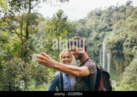 Happy young couple taking self portrait avec leur téléphone cellulaire sur journée de randonnée. Couple taking photo en face d'une cascade. Banque D'Images