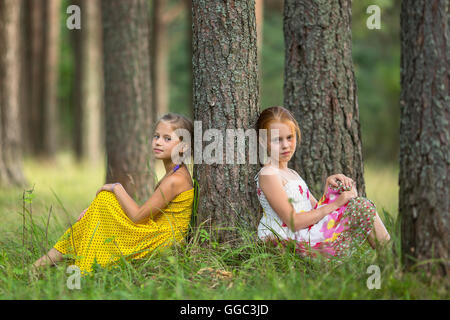 Deux petites filles mignonnes assis près de l'arbre dans une forêt de pins. Banque D'Images