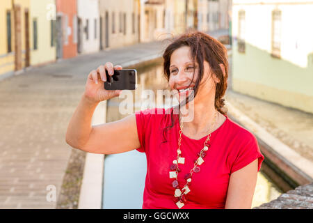 Portrait de l'environnement méditerranéen de femme en robe rouge de prendre une de selfies ancien pont sur canaux d'eau d'un vieux village de l'Italie, Comacchio, connu sous le nom de la Petite Venise Banque D'Images