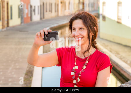 Portrait de l'environnement méditerranéen de femme en robe rouge de prendre une de selfies ancien pont sur canaux d'eau d'un vieux village de l'Italie, Comacchio, connu sous le nom de la Petite Venise, le vent souffle d'un sèche Banque D'Images