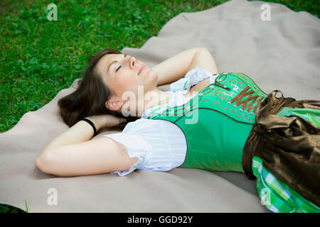 Jeune femme en bavarois dirndl lying on blanket in grass Banque D'Images