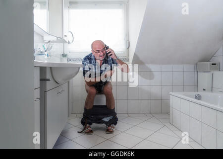 Hauts homme assis sur les toilettes, parlant dans un smartphone, Allemagne Banque D'Images