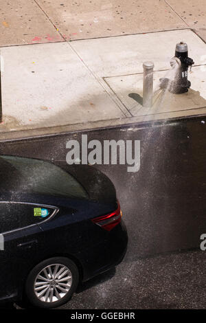 La conduite automobile Toyota de couleur sombre par jets d'eau à partir d'un poteau incendie avec un joint de la buse de pulvérisation Banque D'Images