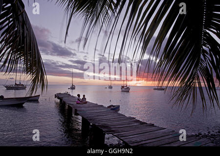 Des enfants assis sur un ponton en bois au bord de la mer dans le coucher du soleil, la Dominique, Lesser Antilles, Caribbean Banque D'Images