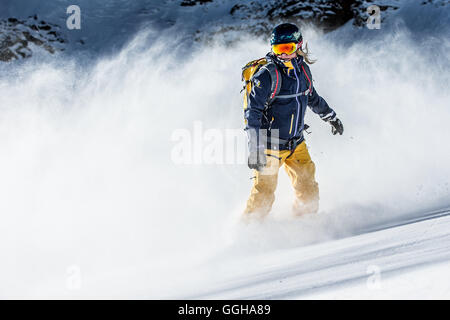 Jeune femme snowboarder équitation à travers la poudreuse profonde dans les montagnes, Pitztal, Tyrol, Autriche Banque D'Images