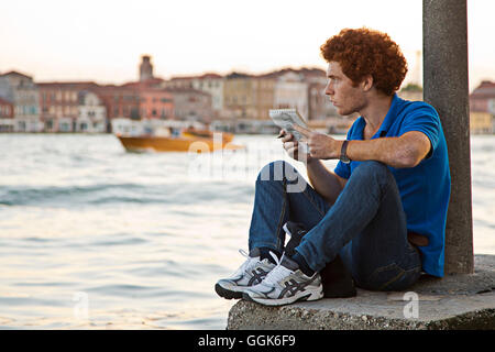 Un jeune homme aux cheveux rouges assis sur les rives de la Canale della Giudecca à Dorsoduro dessin, Venise, Vénétie, Italie, Europe Banque D'Images